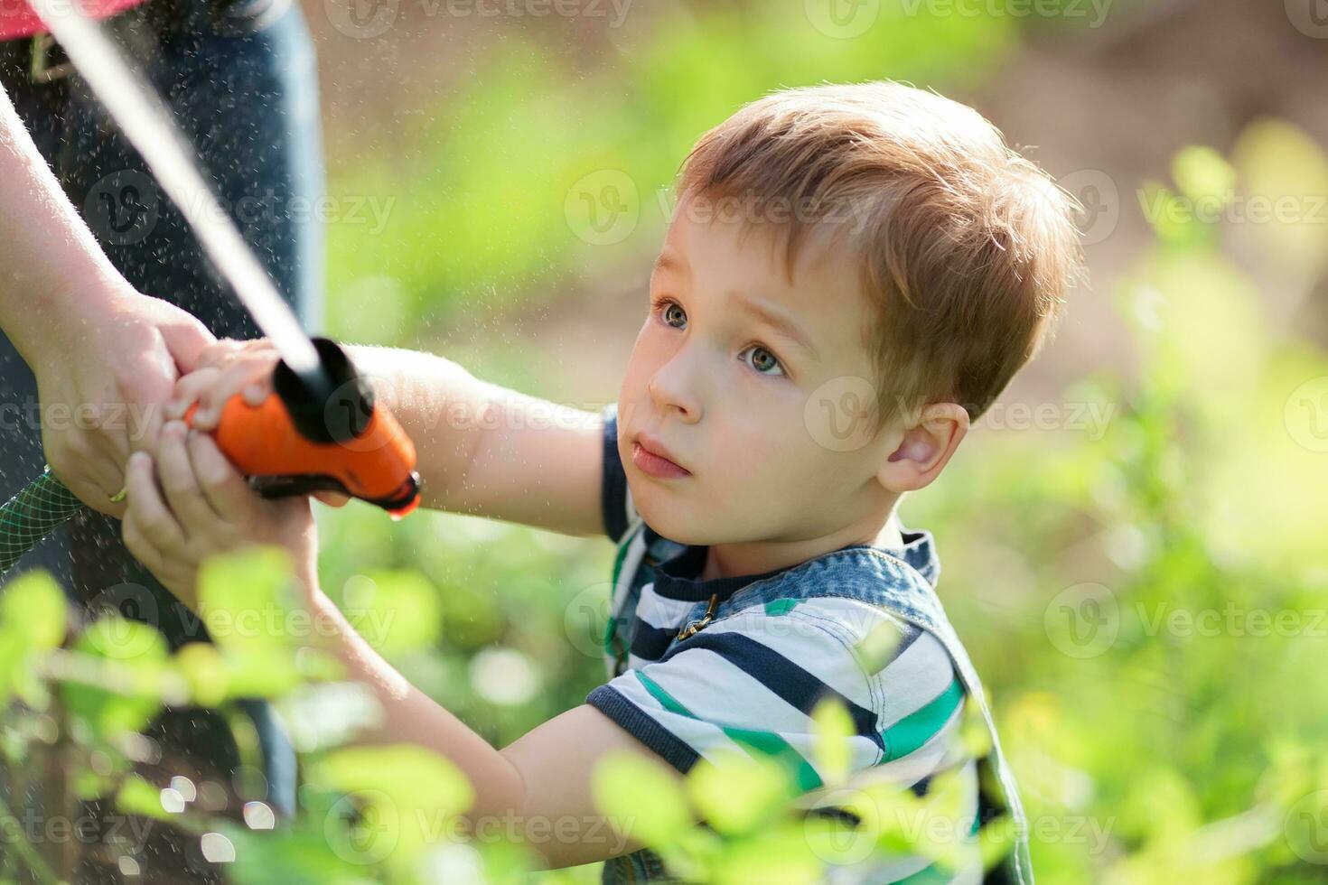 peu garçon en jouant avec une jet de l'eau dans jardin photo