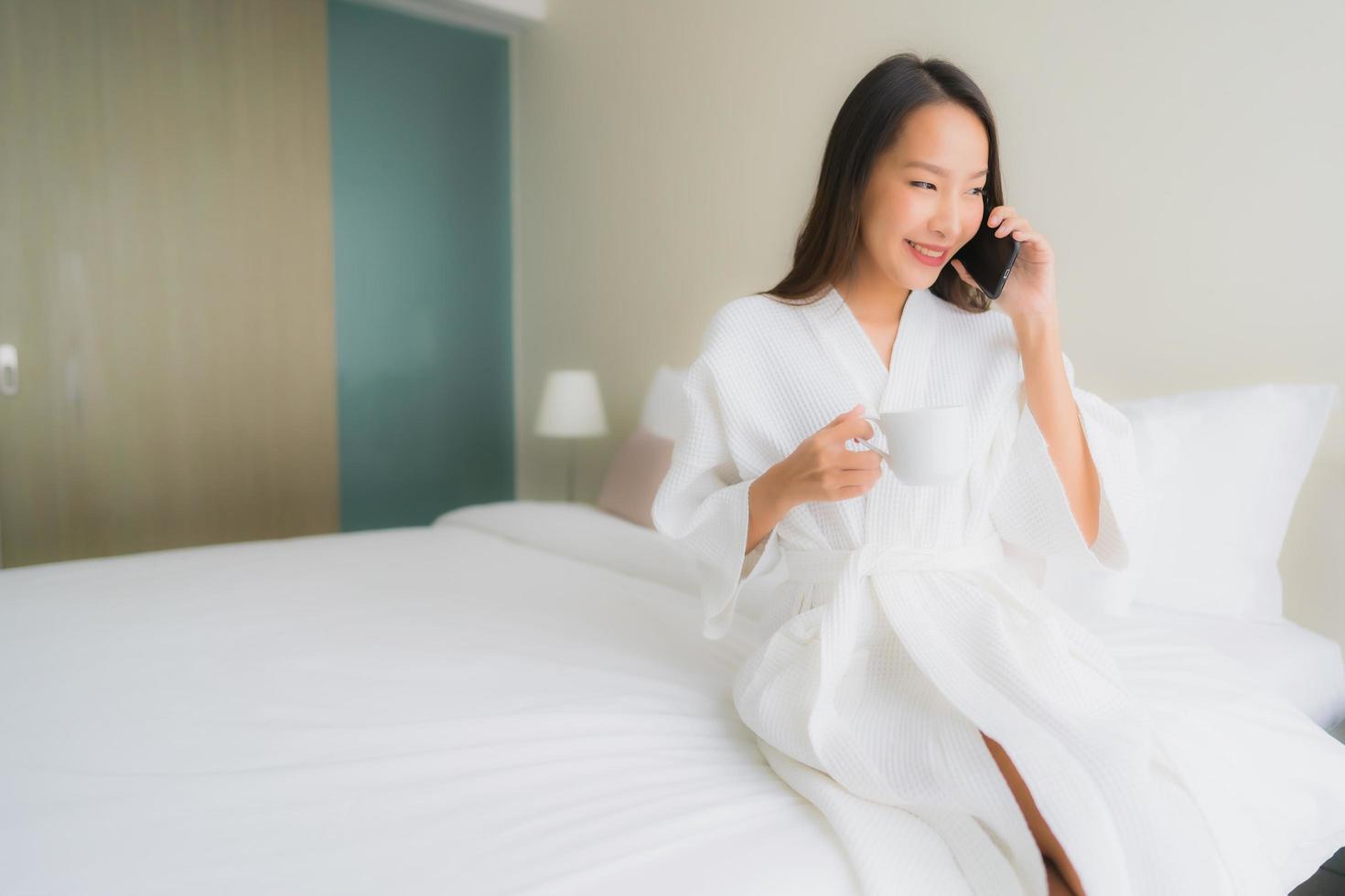 Portrait de belles jeunes femmes asiatiques avec une tasse de café et un téléphone portable sur le lit photo