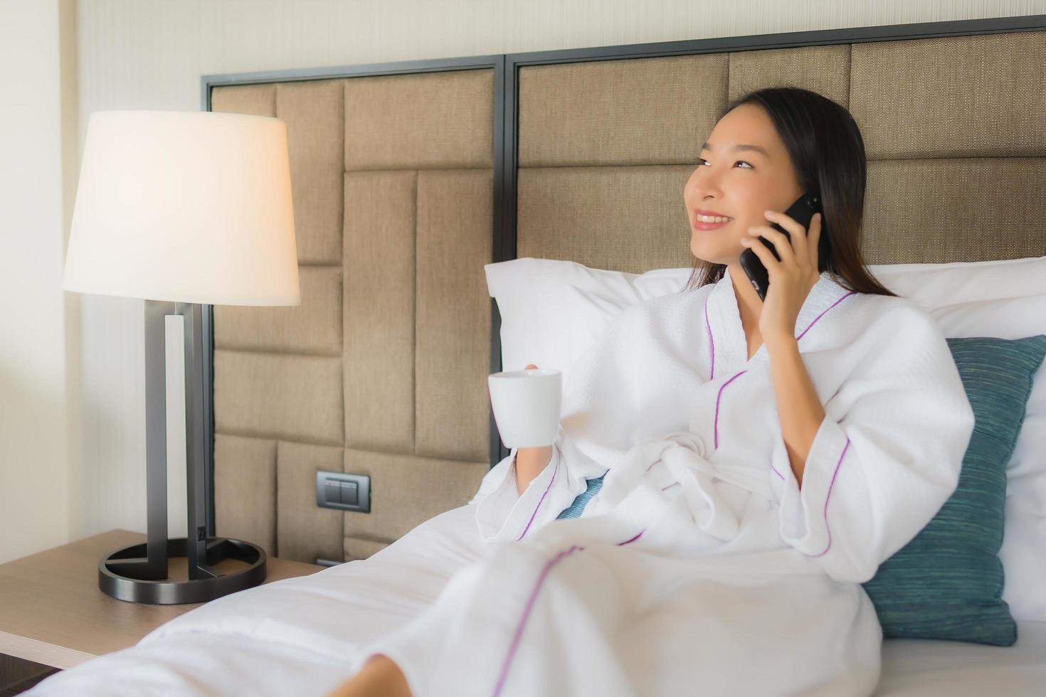 Portrait de belles jeunes femmes asiatiques utilisant un téléphone intelligent mobile avec une tasse de café sur le lit photo