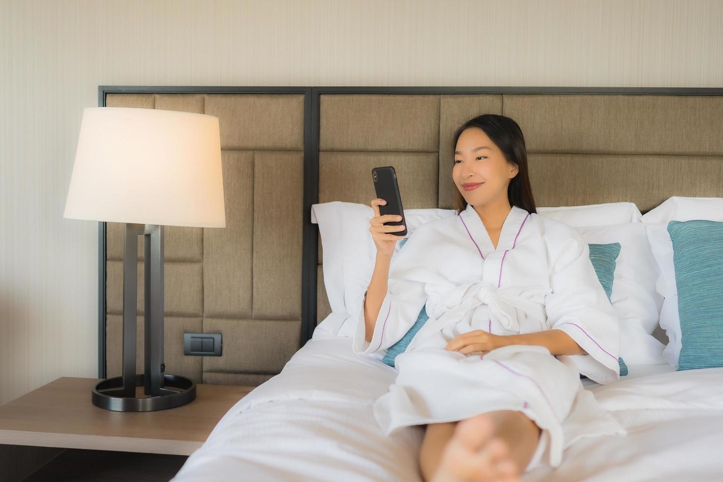 Portrait de belles jeunes femmes asiatiques utilisant un téléphone intelligent mobile avec une tasse de café sur le lit photo
