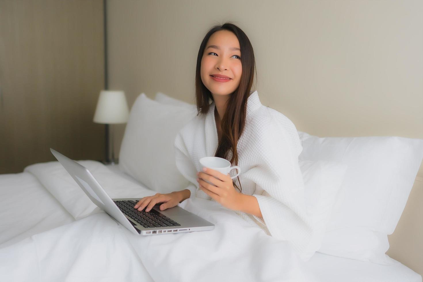 Portrait de belles jeunes femmes asiatiques avec une tasse de café et un ordinateur portable sur le lit photo