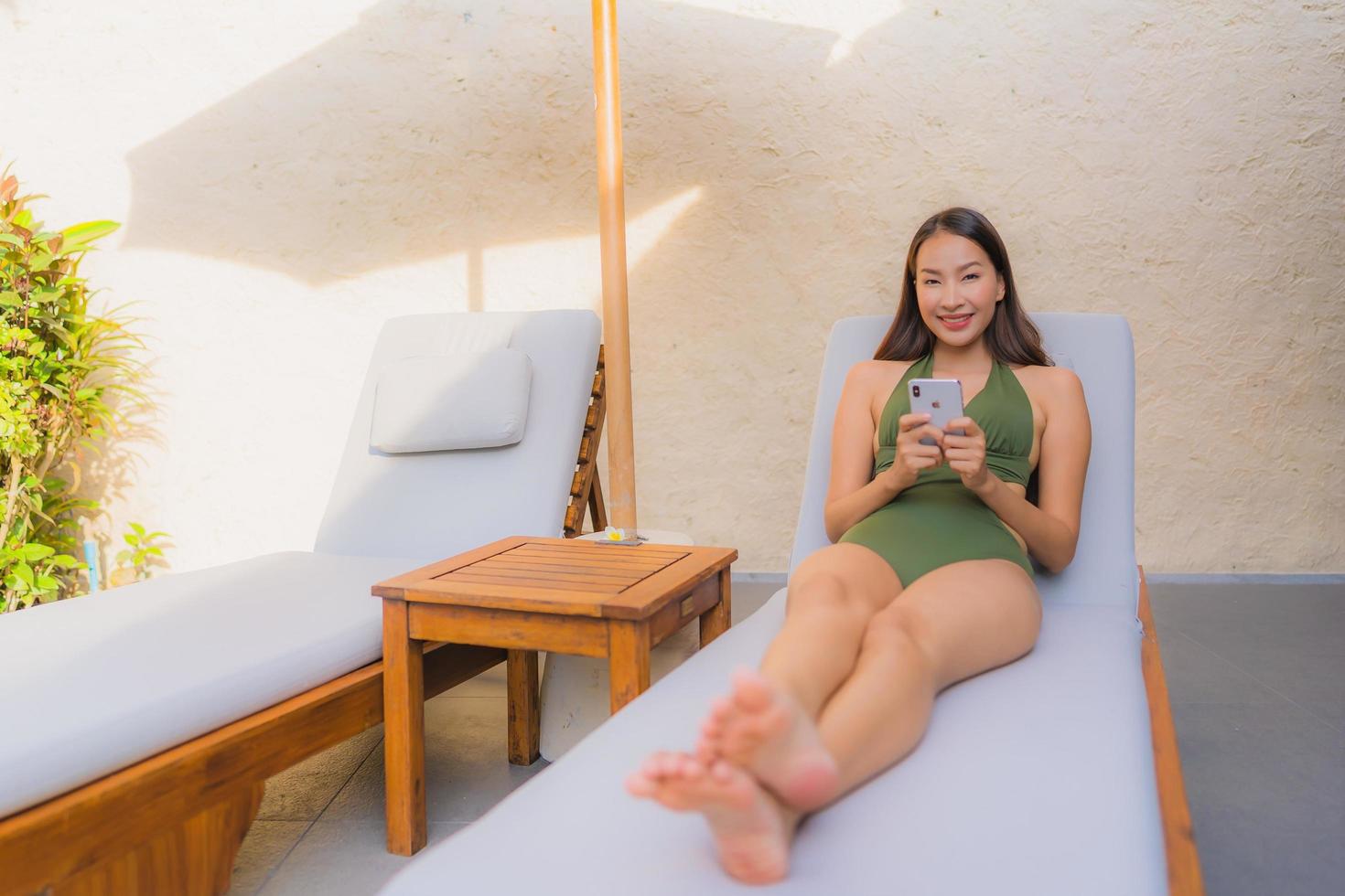 Portrait belle jeune femme asiatique assise sur la chaise longue avec parasol près de la piscine photo