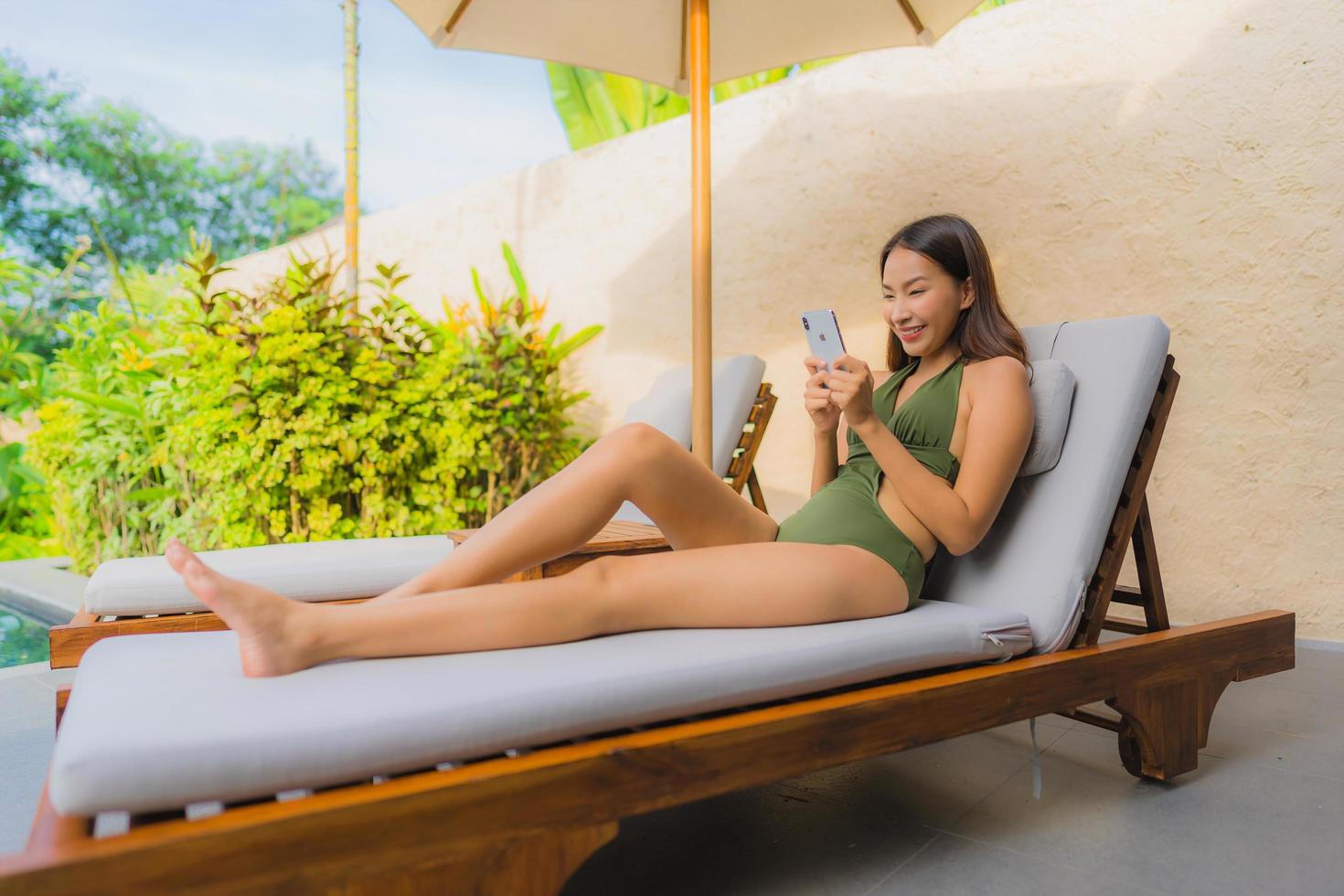 Portrait belle jeune femme asiatique assise sur la chaise longue avec parasol près de la piscine photo