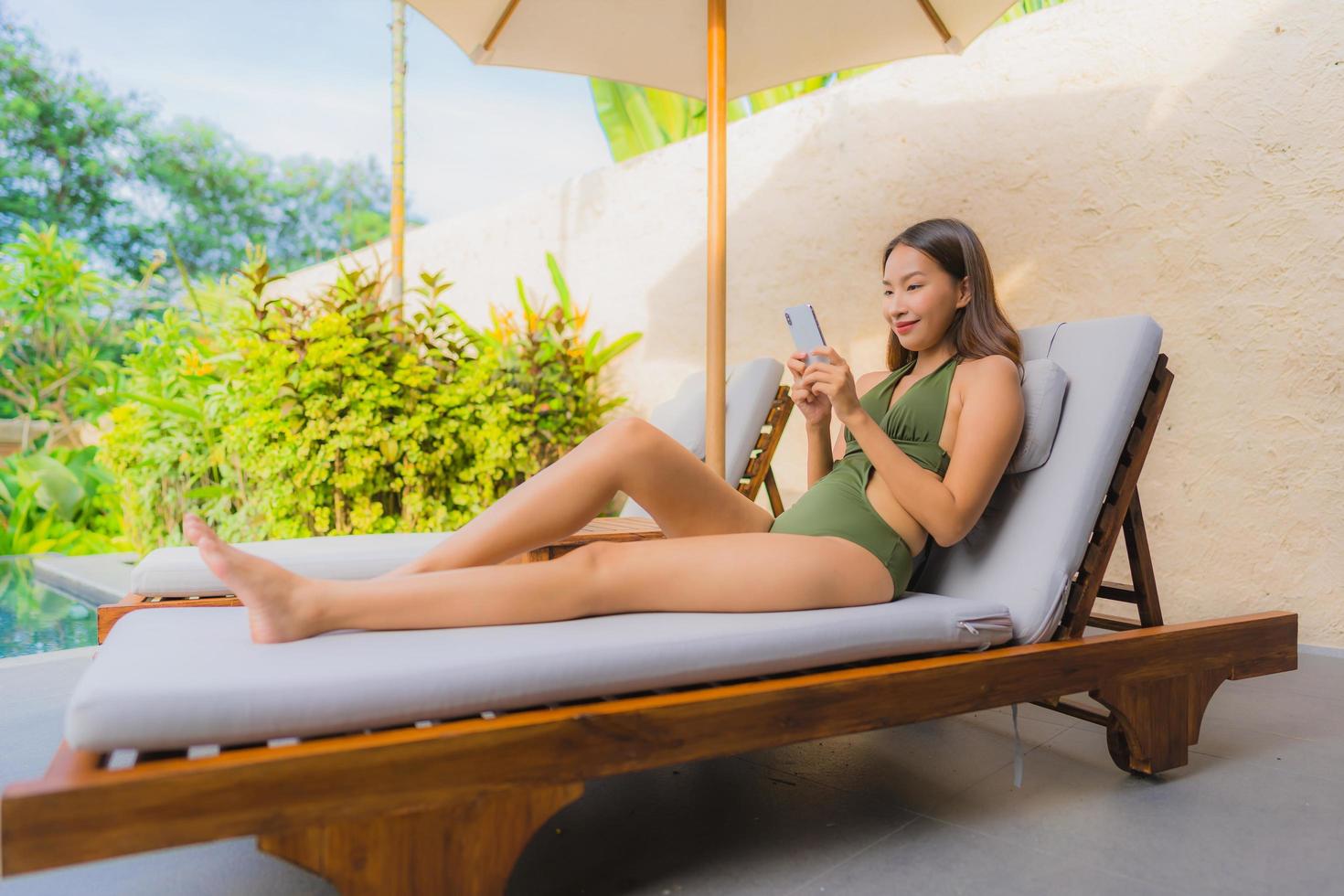 Portrait belle jeune femme asiatique assise sur la chaise longue avec parasol près de la piscine photo