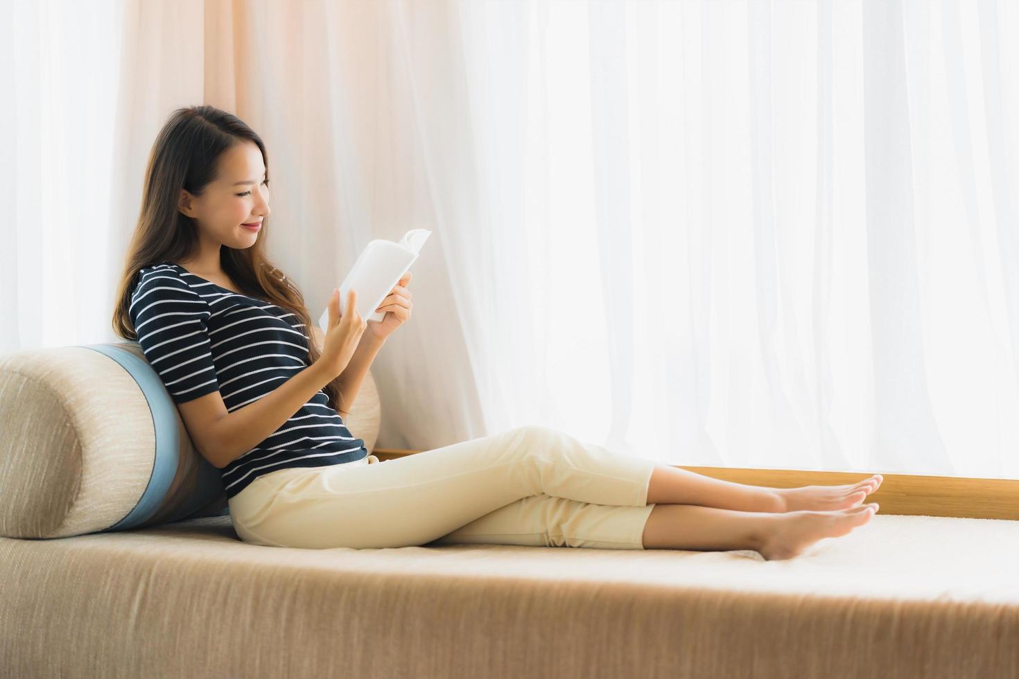 Portrait belle jeune femme asiatique lisant un livre sur un canapé dans le salon photo