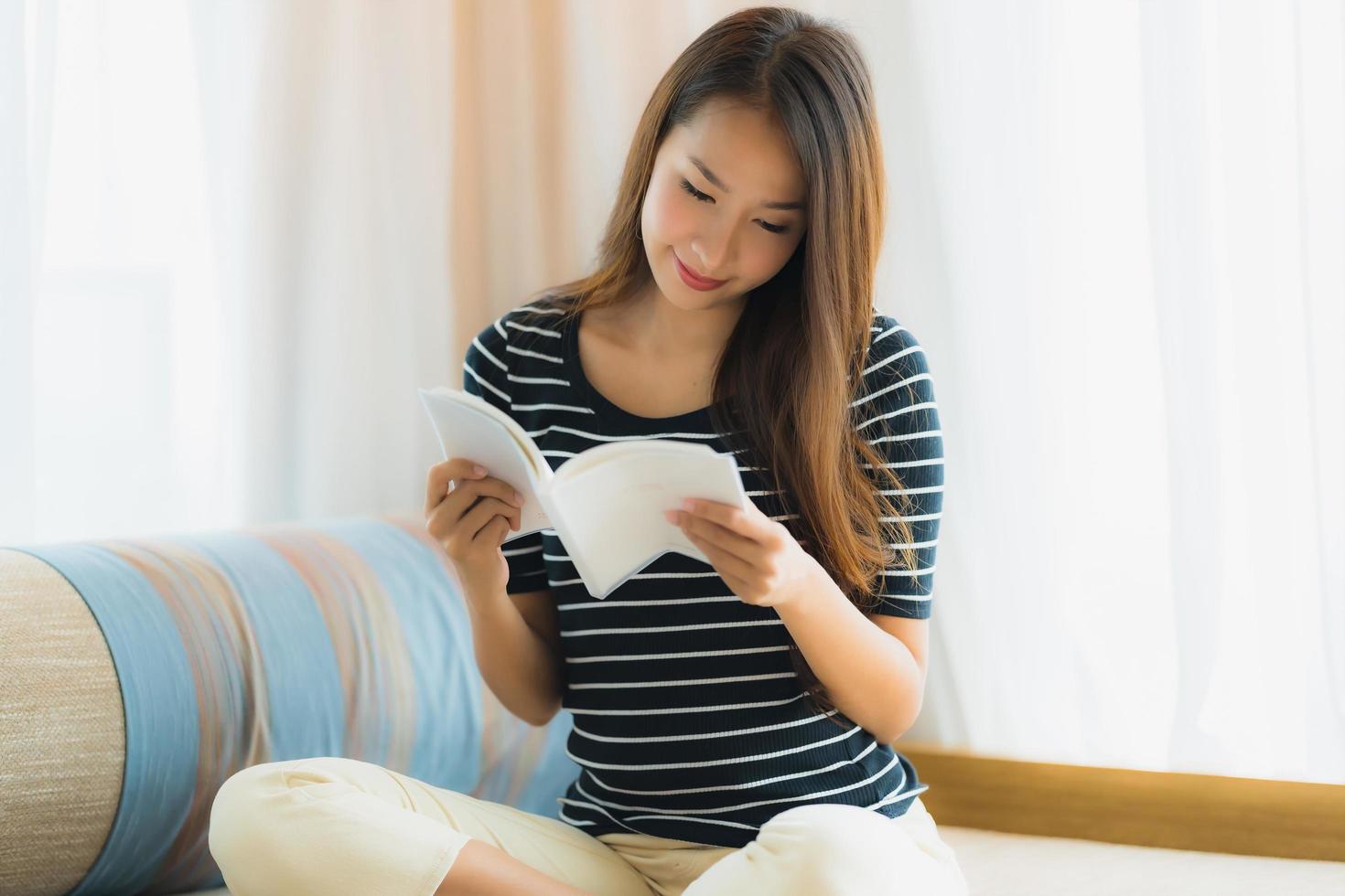 Portrait belle jeune femme asiatique lisant un livre sur un canapé dans le salon photo