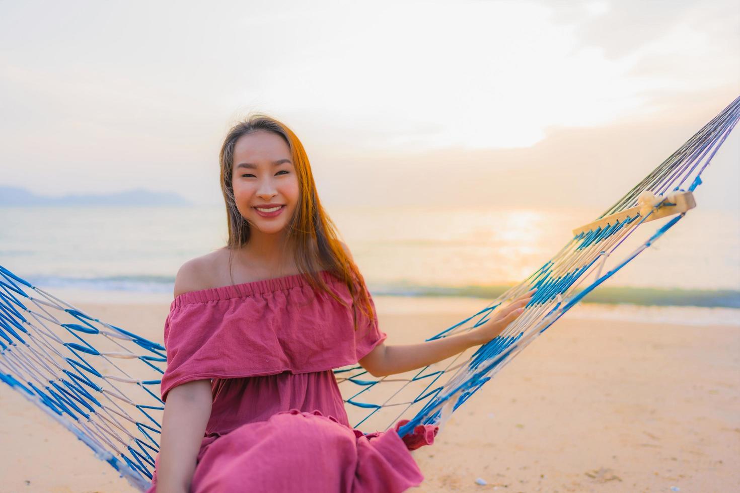 Portrait belle jeune femme asiatique assise sur le hamac avec sourire heureux plage proche mer et océan photo