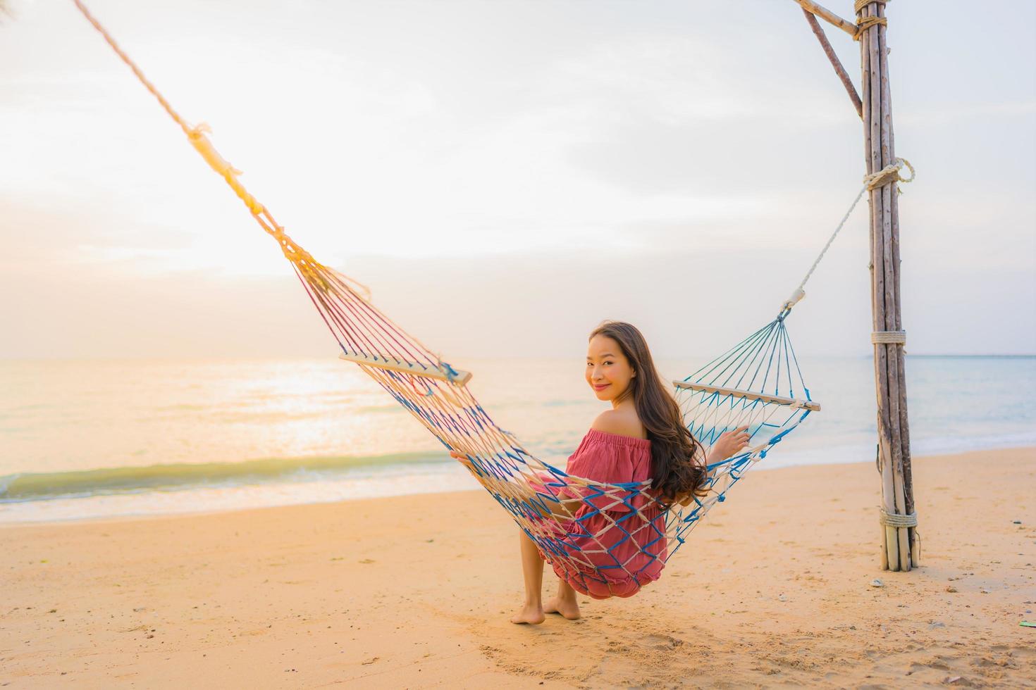 Portrait belle jeune femme asiatique assise sur le hamac avec sourire heureux plage proche mer et océan photo