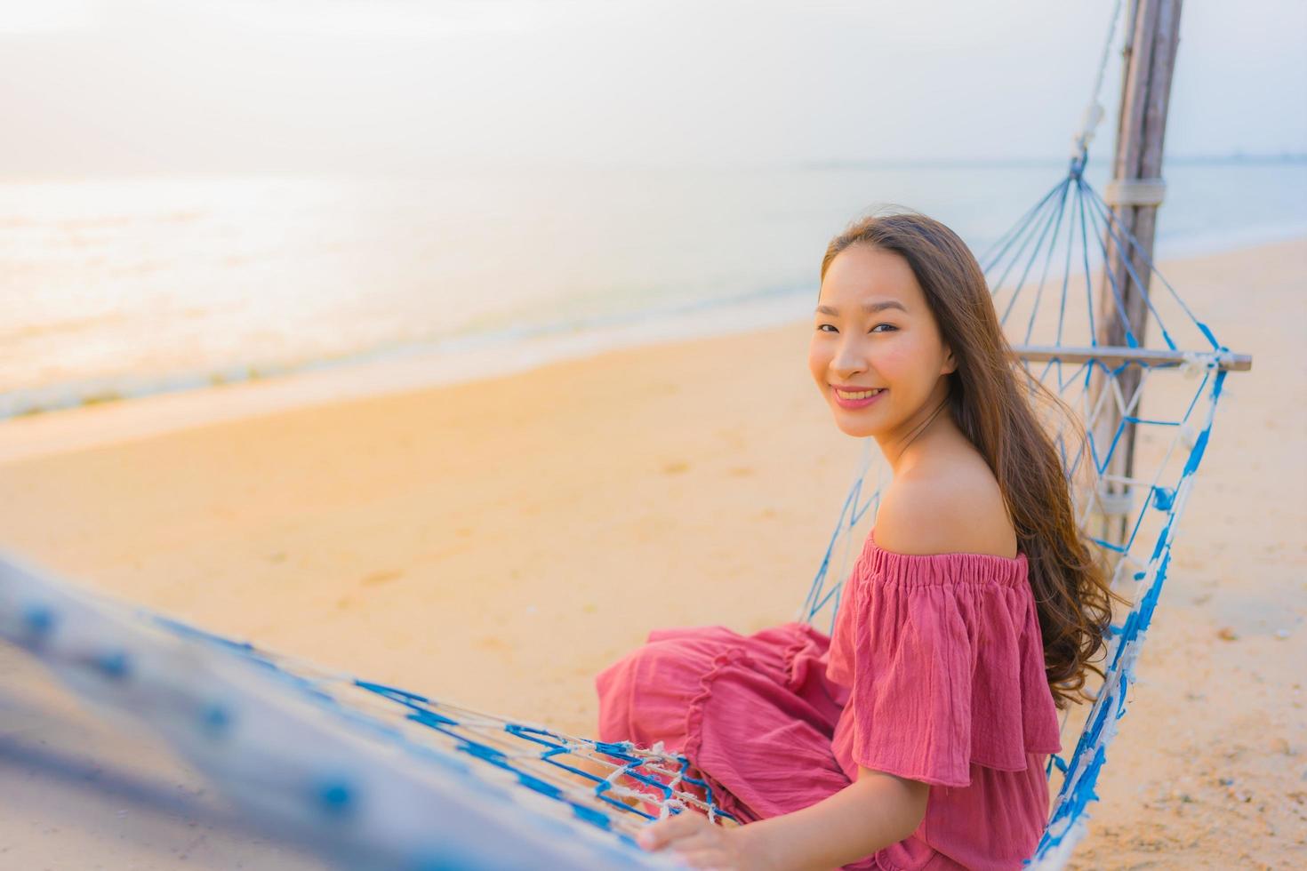 Portrait belle jeune femme asiatique assise sur le hamac avec sourire heureux plage proche mer et océan photo