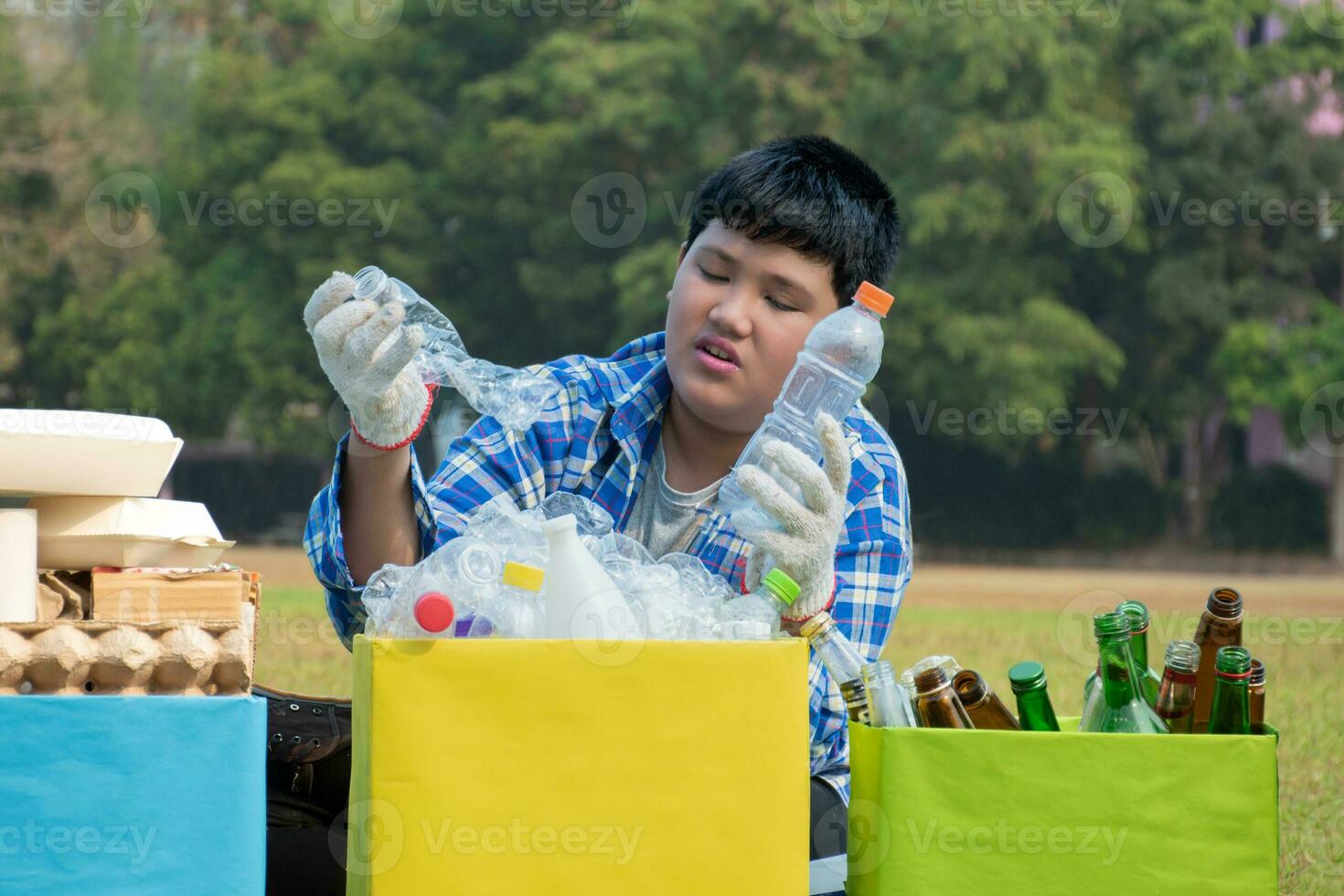 asiatique garçon dans plaid chemise séance sur terrain de jeux de école avec divers des boites de séparé les ordures ou poubelles à l'intérieur, concept pour éco copains et global chauffage campagne, doux et sélectif se concentrer. photo