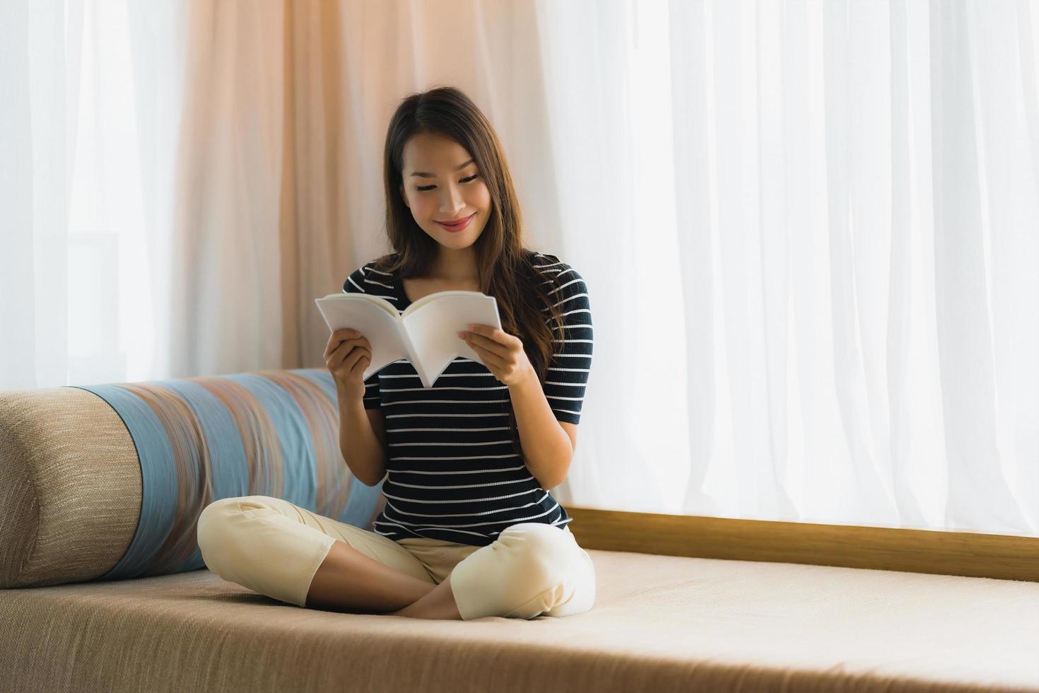 Portrait belle jeune femme asiatique lisant un livre sur un canapé dans le salon photo