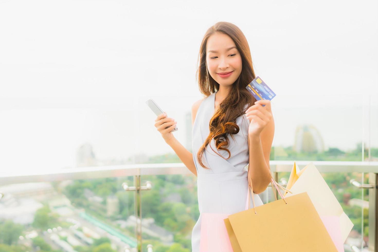 portrait belle jeune femme asiatique heureuse et souriante avec carte de crédit et téléphone portable ou intelligent et sac à provisions photo