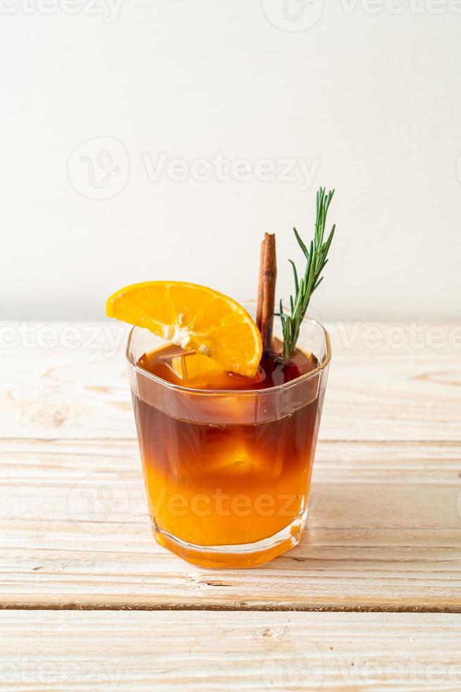 un verre de café noir americano glacé et une couche de jus d'orange et de citron décoré de romarin et de cannelle sur fond de bois photo