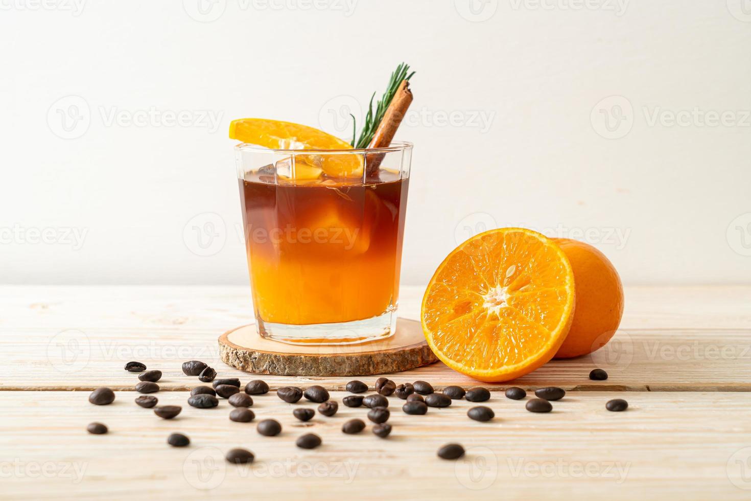 un verre de café noir americano glacé et une couche de jus d'orange et de citron décoré de romarin et de cannelle sur fond de bois photo