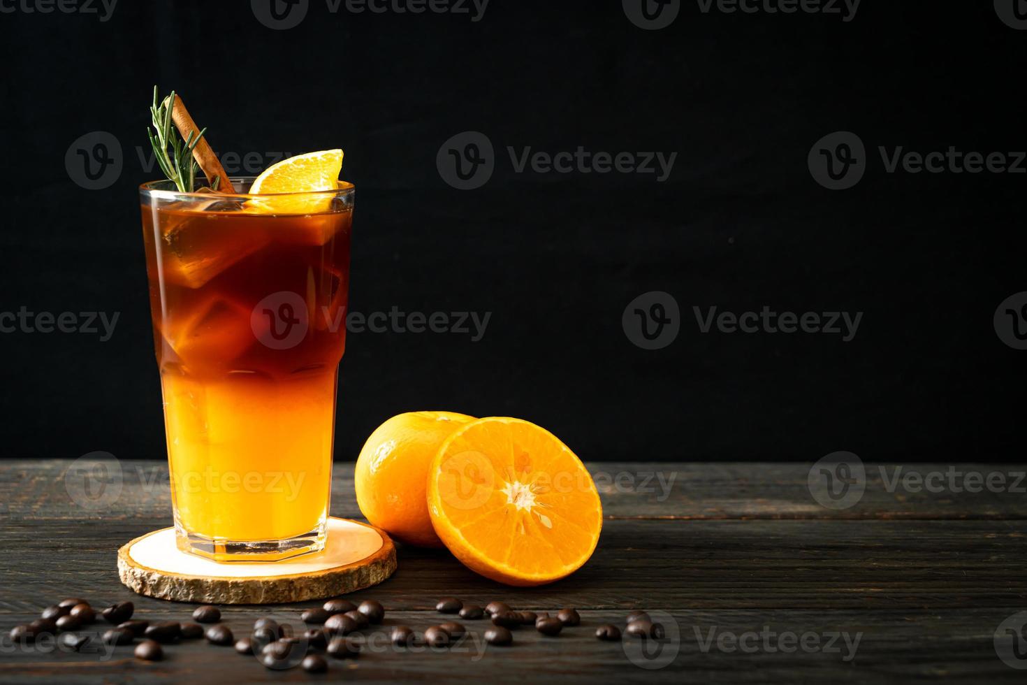 un verre de café noir americano glacé et une couche de jus d'orange et de citron décoré de romarin et de cannelle sur fond de bois photo