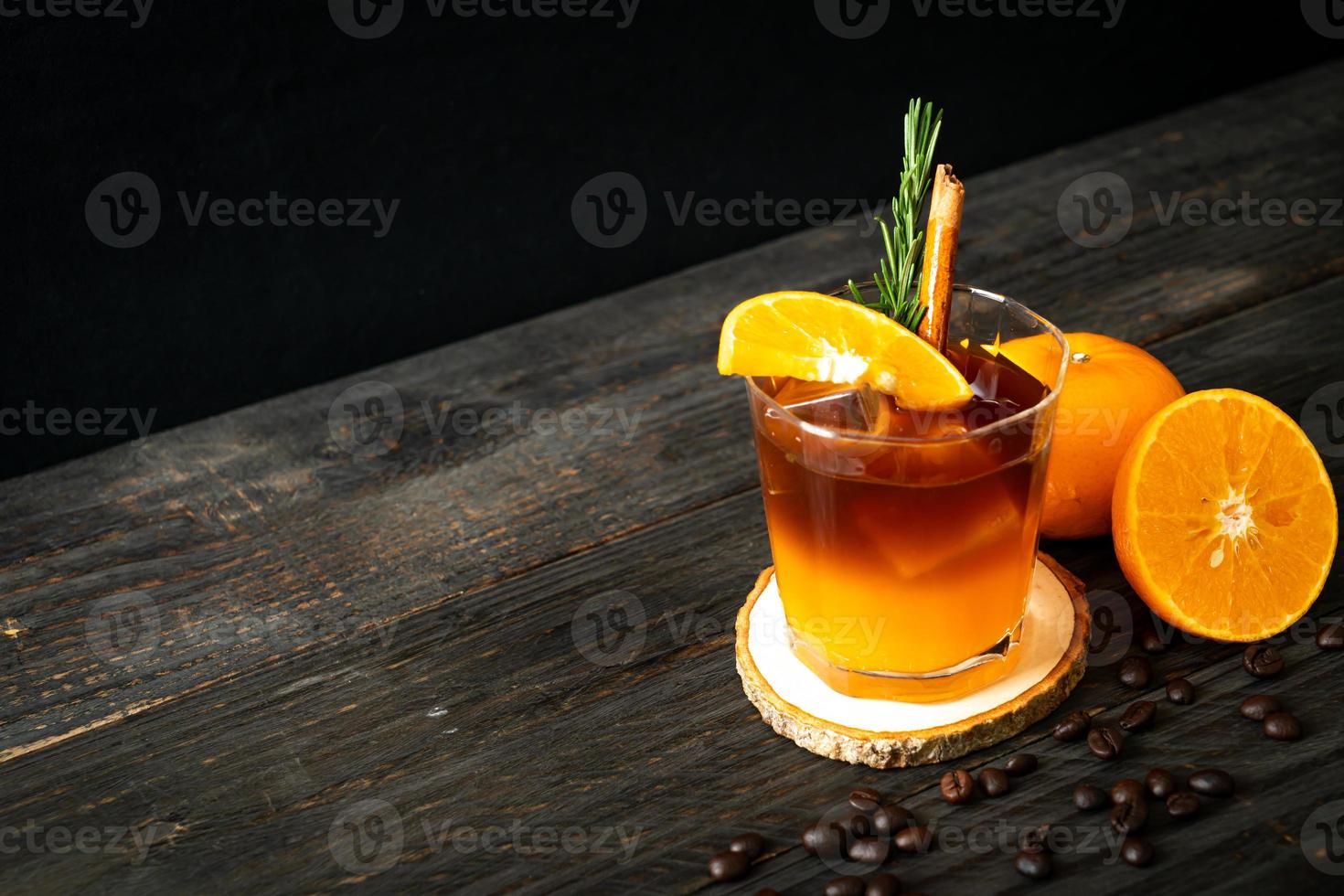 un verre de café noir americano glacé et une couche de jus d'orange et de citron décoré de romarin et de cannelle sur fond de bois photo