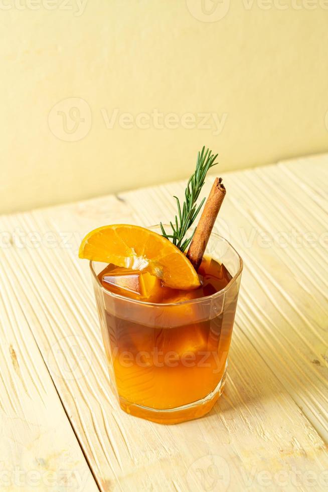 un verre de café noir americano glacé et une couche de jus d'orange et de citron décoré de romarin et de cannelle sur fond de bois photo