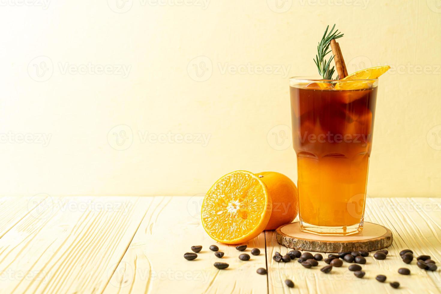 un verre de café noir americano glacé et une couche de jus d'orange et de citron décoré de romarin et de cannelle sur fond de bois photo