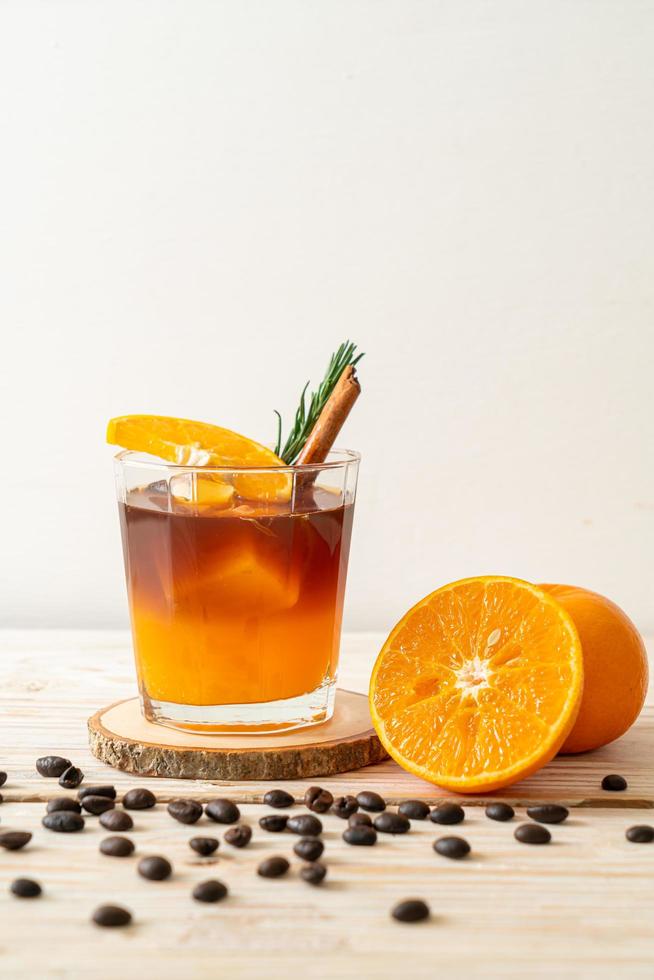 un verre de café noir americano glacé et une couche de jus d'orange et de citron décoré de romarin et de cannelle sur fond de bois photo