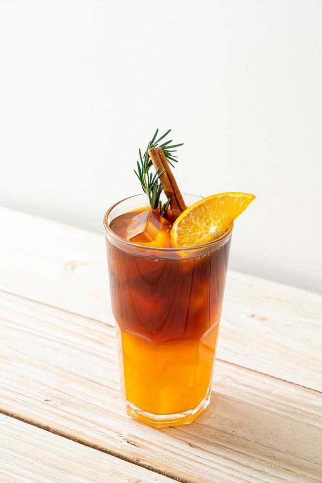 un verre de café noir americano glacé et une couche de jus d'orange et de citron décoré de romarin et de cannelle sur fond de bois photo
