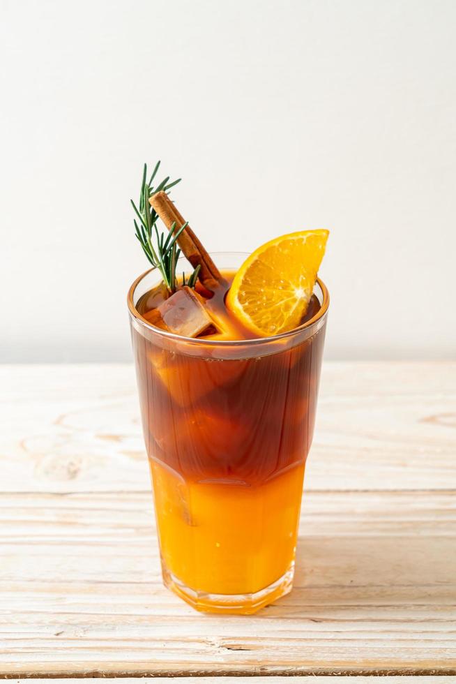 un verre de café noir americano glacé et une couche de jus d'orange et de citron décoré de romarin et de cannelle sur fond de bois photo