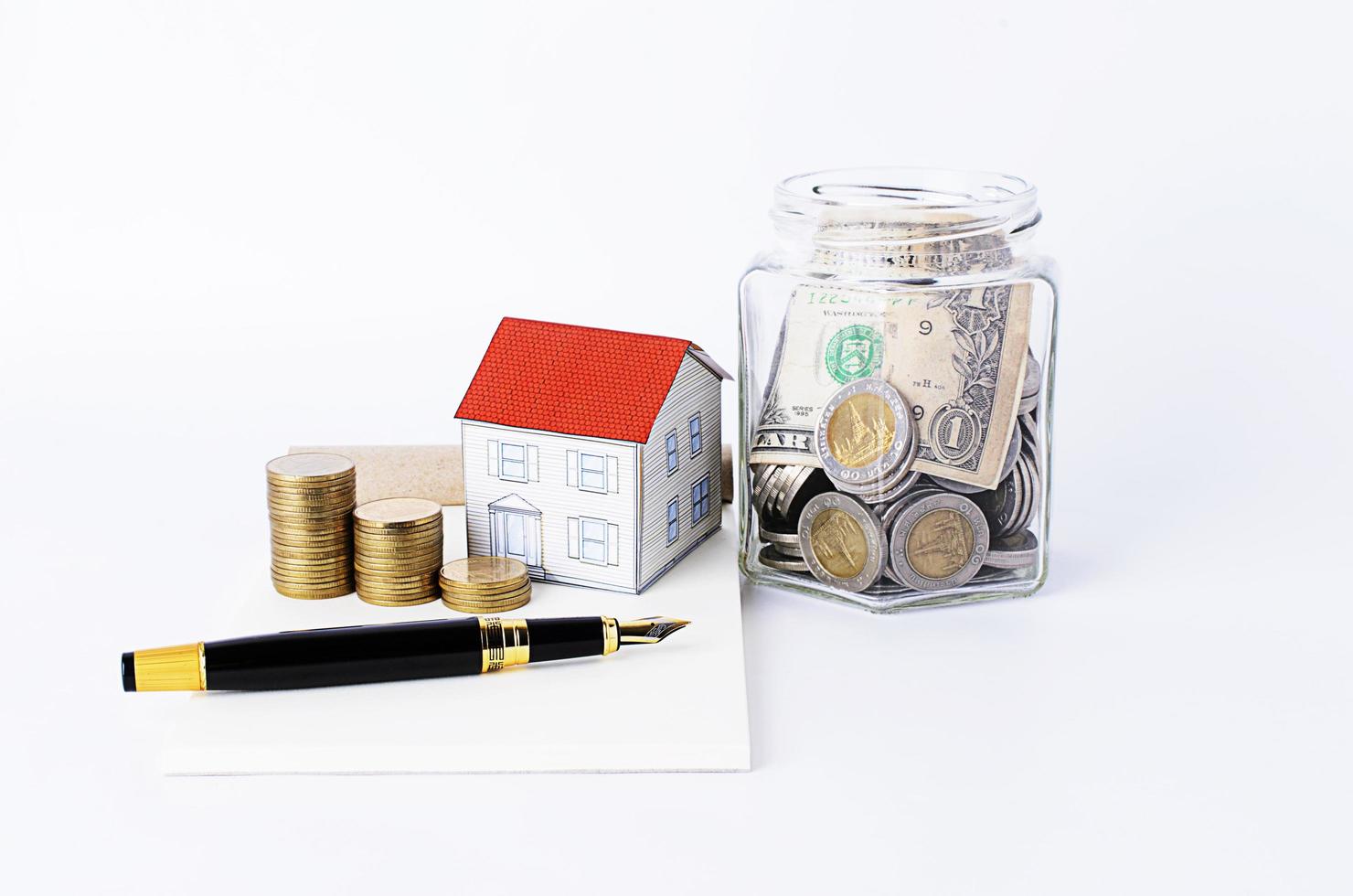 stylo plume avec pile de pièces de monnaie et maison de papier et banque de bouteilles photo