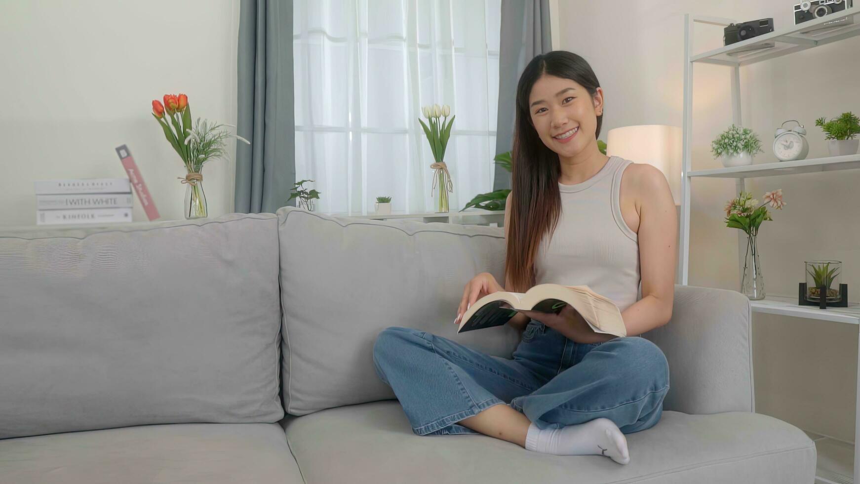 magnifique asiatique Jeune femme en train de lire livre sur canapé à maison. photo