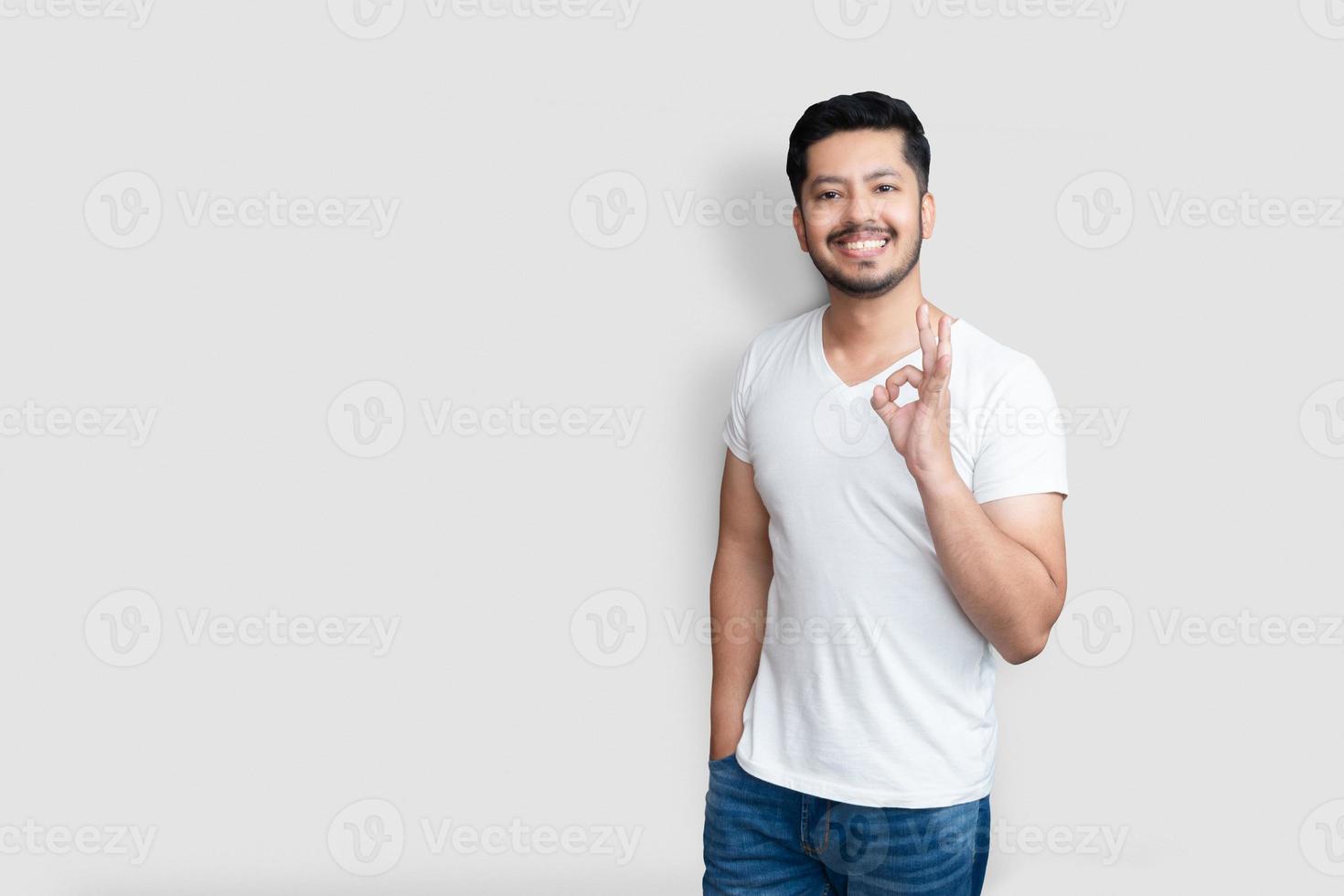 concept de langage corporel. beau mec asiatique créatif avec une barbe légère, levant la main dans un geste d'accord et souriant tout en appréciant le plan isolé sur fond blanc photo