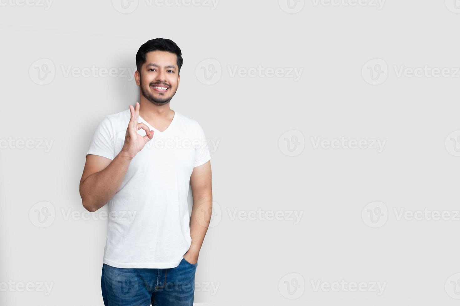 concept de langage corporel. beau mec asiatique créatif avec une barbe légère, levant la main dans un geste d'accord et souriant tout en appréciant le plan isolé sur fond blanc photo