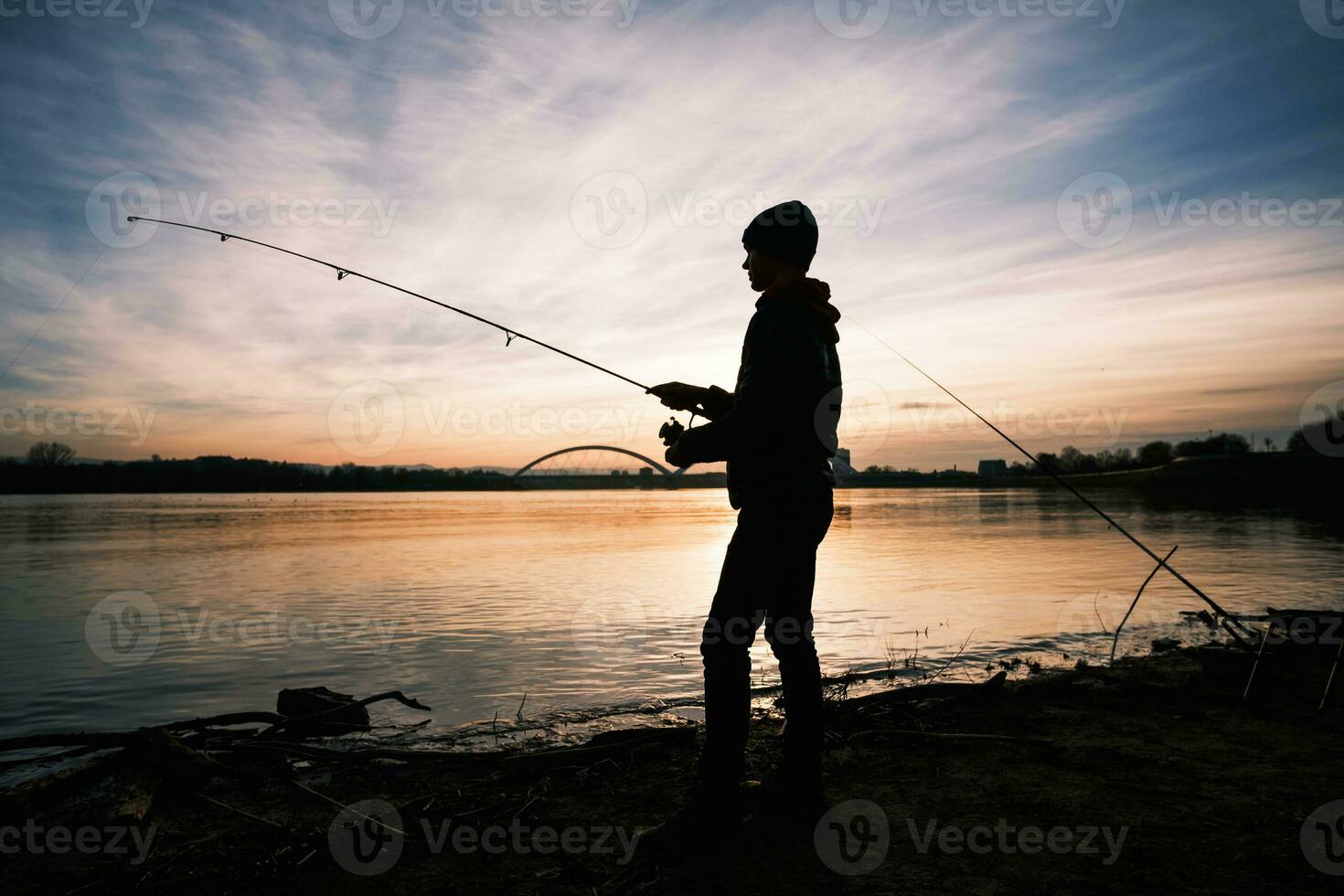 adolescent garçon est pêche sur rivière banque. garçon est pêche dans le coucher du soleil. photo