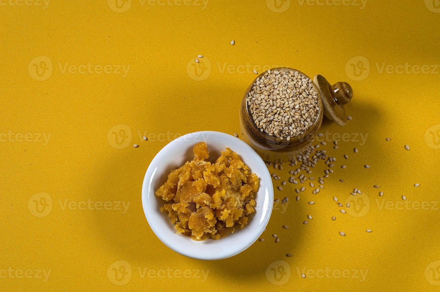 graines de sésame dans un pot en argile avec jaggery dans un bol sur fond jaune photo