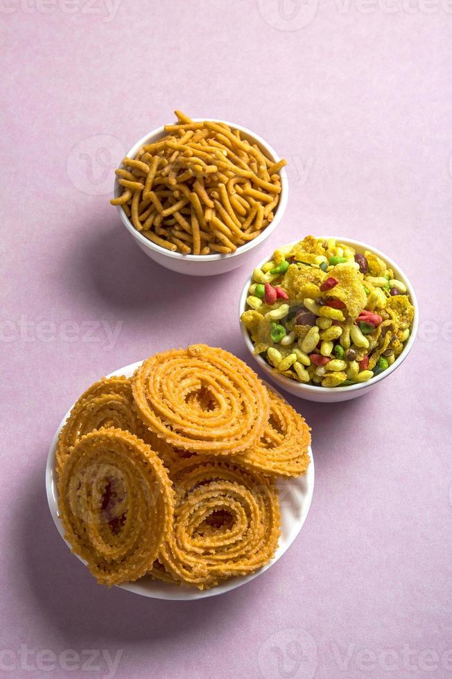 snack indien chakli, chakali ou murukku et farine de gramme besan sev et chivada ou chiwada sur fond rose. nourriture de diwali photo