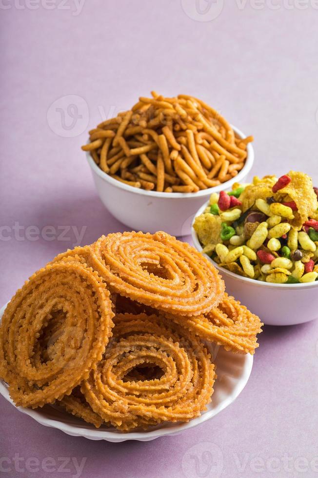 snack indien chakli, chakali ou murukku et farine de gramme besan sev et chivada ou chiwada sur fond rose. nourriture de diwali photo