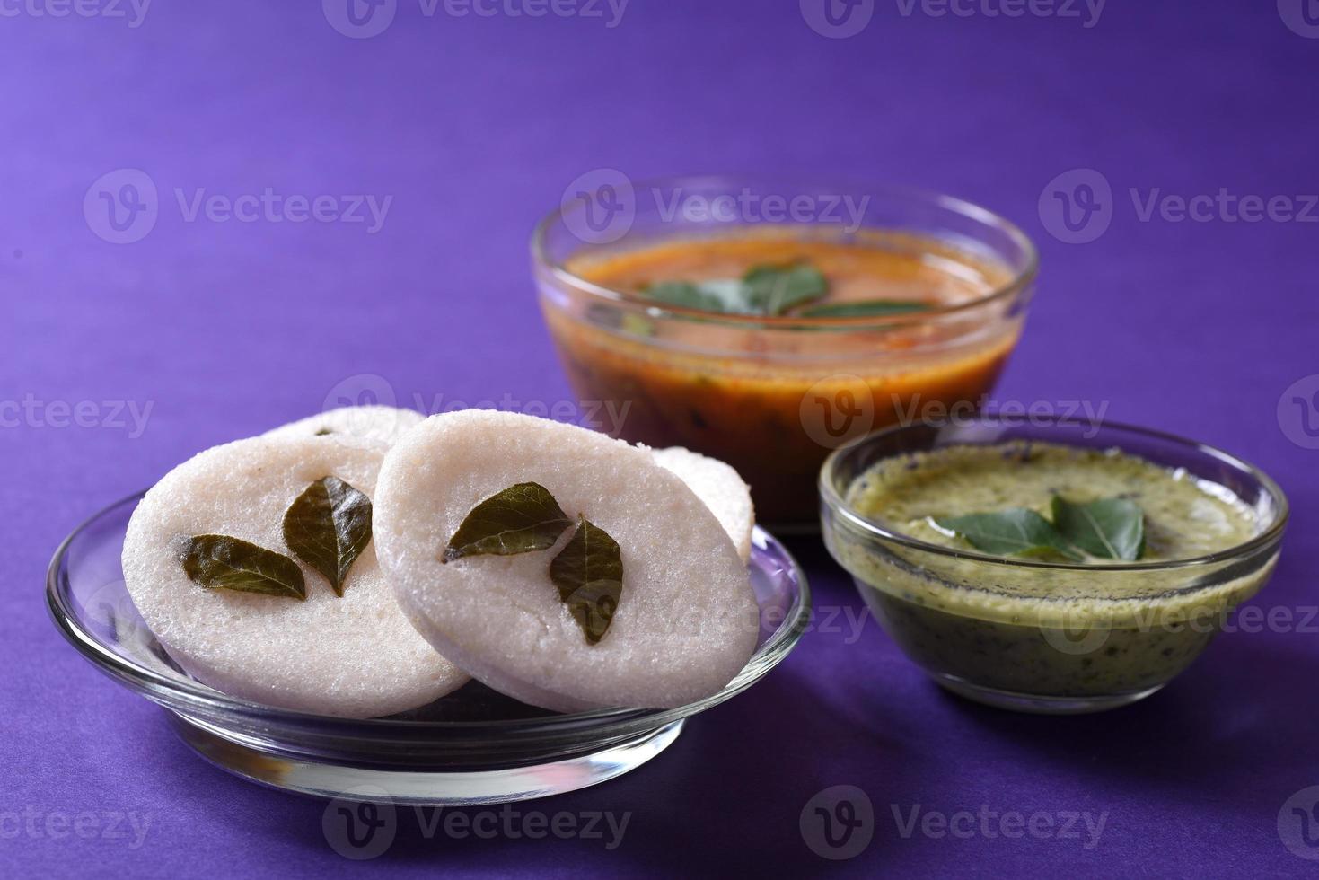 idli avec sambar et chutney de noix de coco sur fond violet, plat indien plat préféré de l'Inde du Sud rava idli ou semoule oisivement ou rava oisivement, servi avec du sambar et du chutney vert. photo