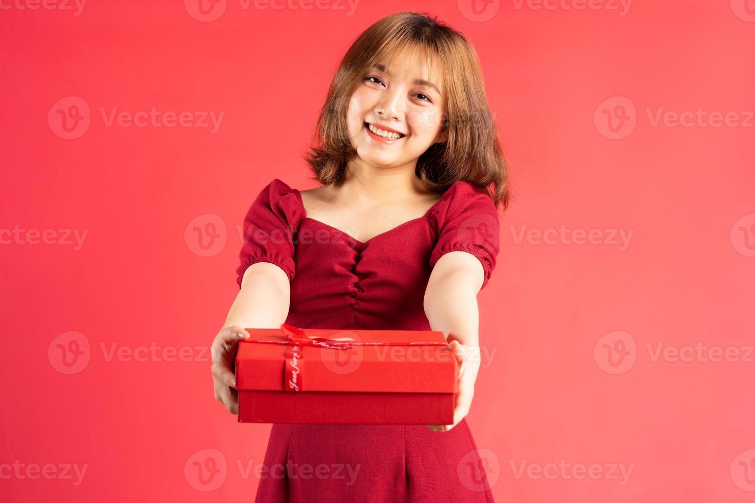 jeune fille asiatique en robe tenant une boîte cadeau rouge avec une expression joyeuse sur fond photo