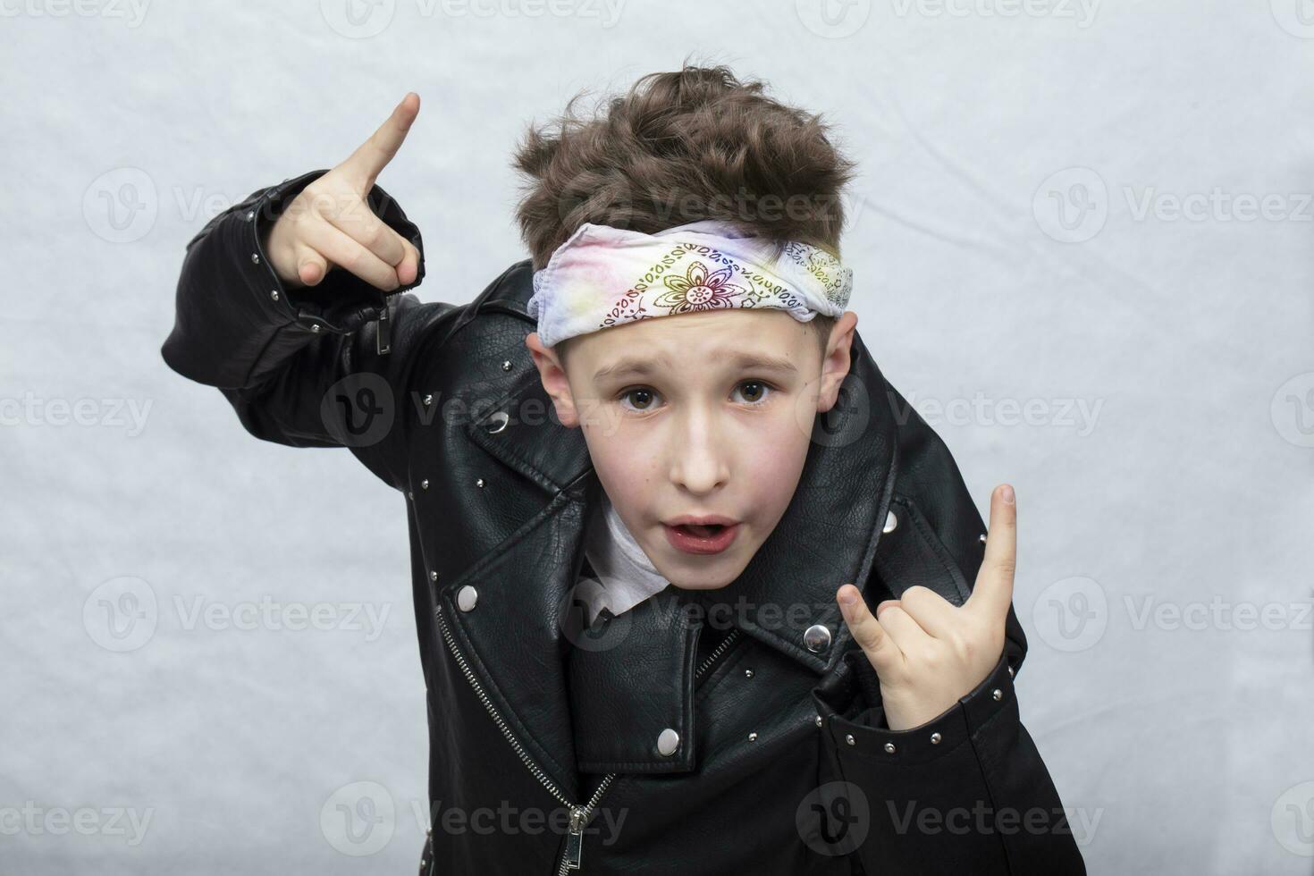 portrait de une lourd métal garçon dans des lunettes de soleil. mignonne adolescent dans une cuir veste Faire une Roche et rouleau signe photo