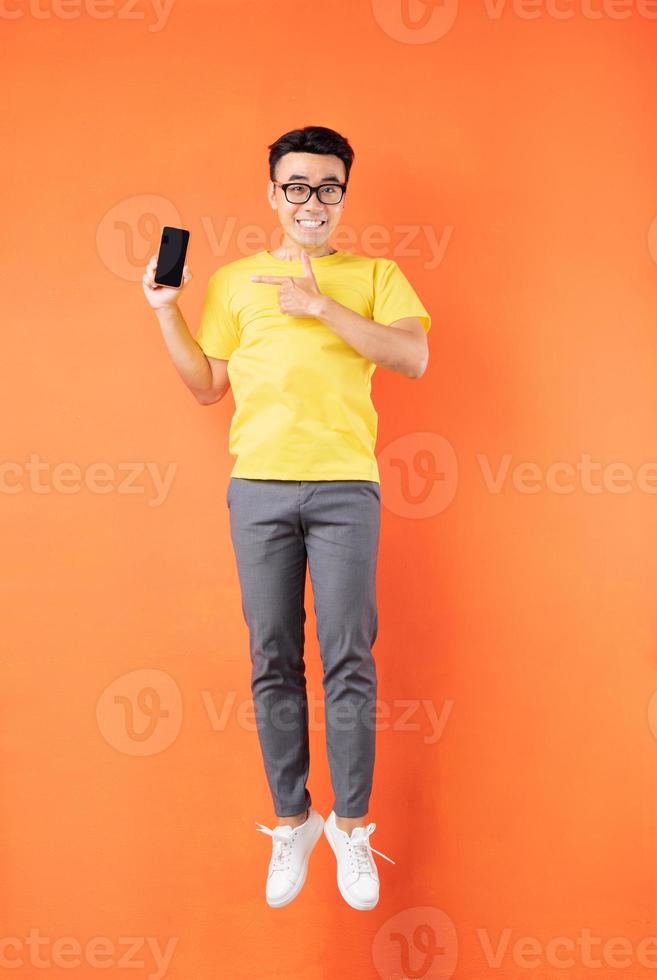 homme asiatique en t-shirt jaune sautant sur fond orange photo