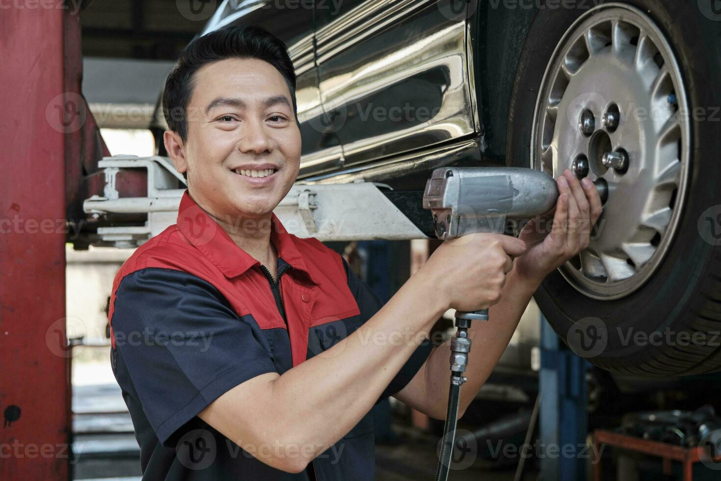 un expert asiatique Masculin automobile mécanicien technicien est baise voiture roue des noisettes sur levage avec percer clé pour réparation à garage. véhicule entretien un service travaux industrie Occupation affaires emplois. photo