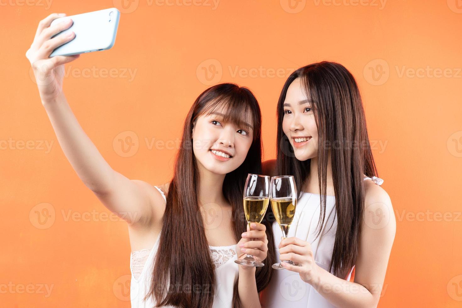 deux belles jeunes filles asiatiques soulevant des verres à vin sur fond orange photo