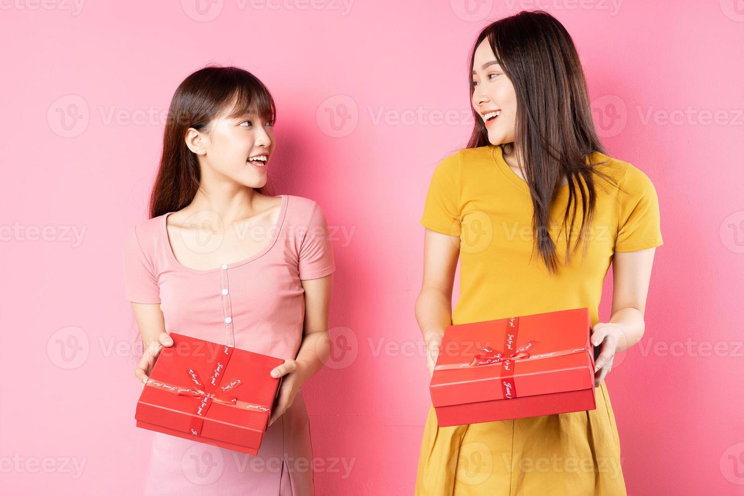 portrait de deux belles jeunes filles asiatiques tenant une boîte cadeau rouge sur fond rose photo