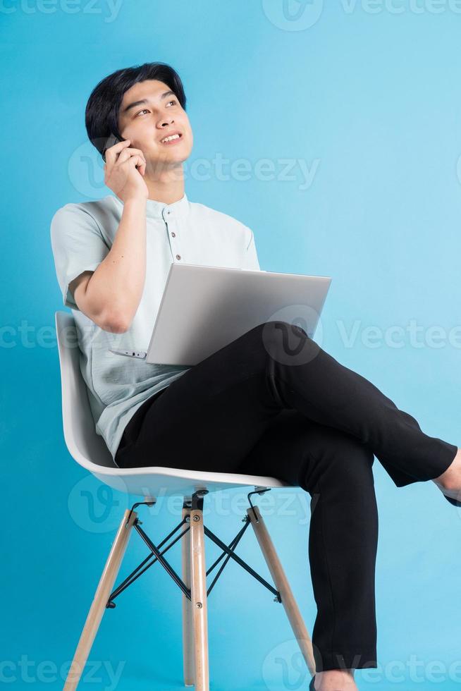 homme asiatique assis sur une chaise tout en utilisant un ordinateur portable tout en passant un appel photo