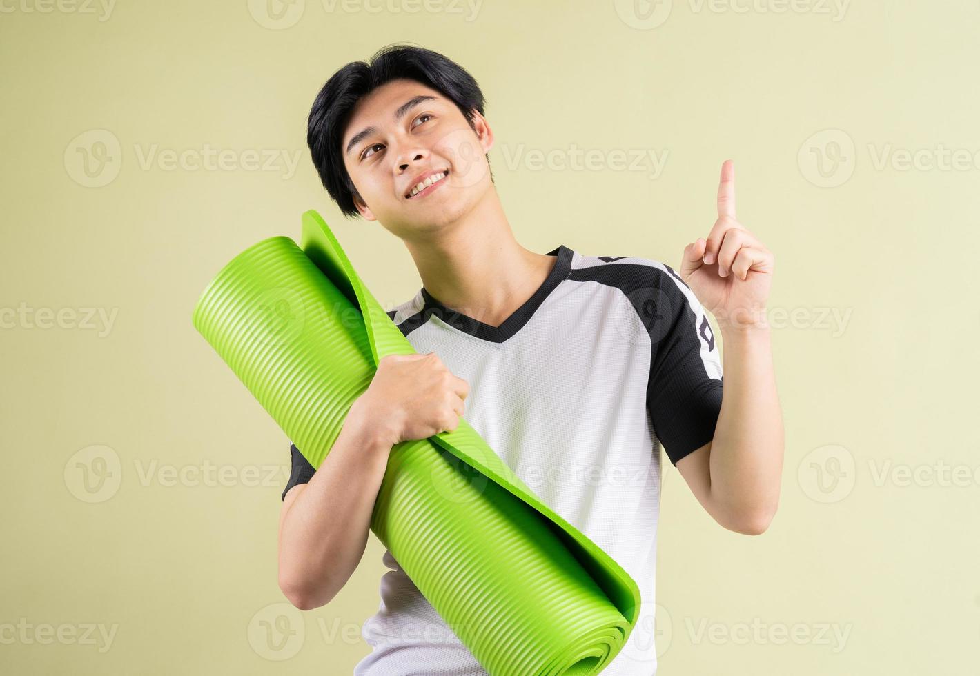 homme asiatique tenant un tapis de yoga sur fond bleu photo