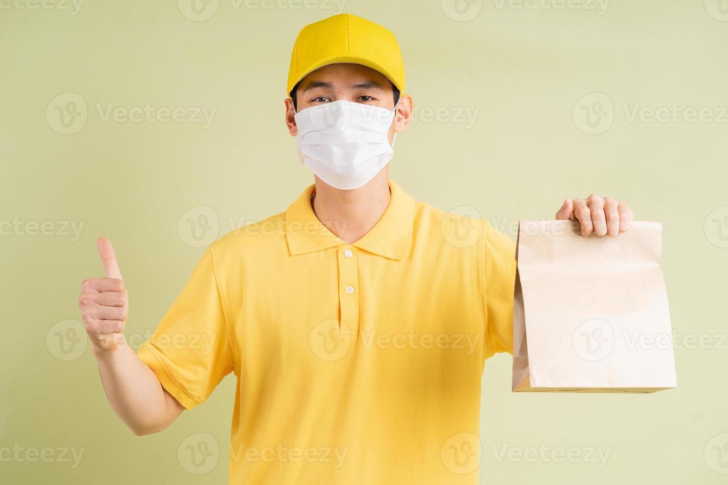 le livreur asiatique masqué tenait le sac en papier et tenait son pouce photo