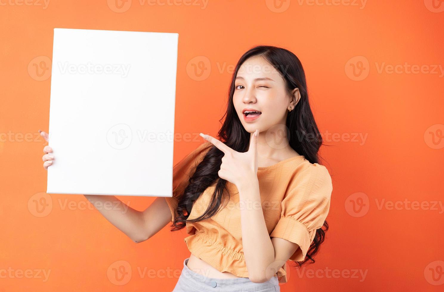Jeune femme asiatique tenant un tableau blanc sur fond orange photo