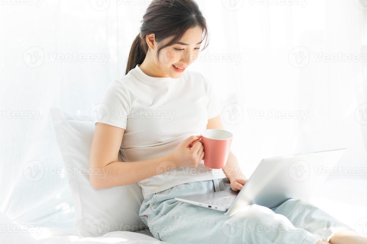jeune femme asiatique assise sur le lit travaillant en regardant le divertissement à domicile photo