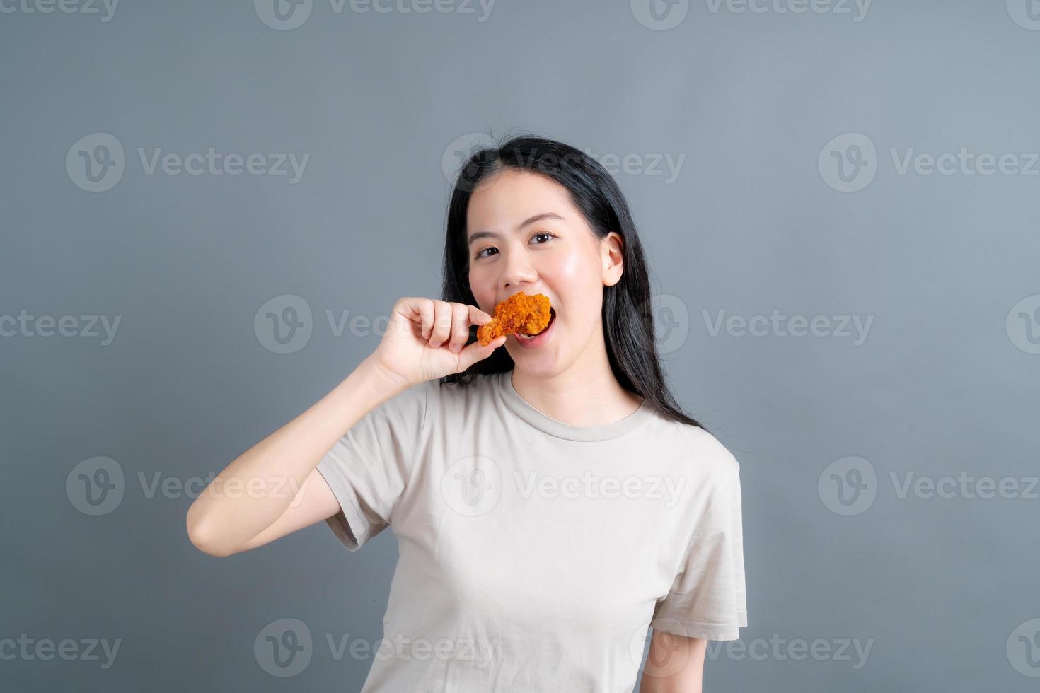 jeune femme asiatique portant un pull avec un visage heureux et aime manger du poulet frit sur fond gris photo