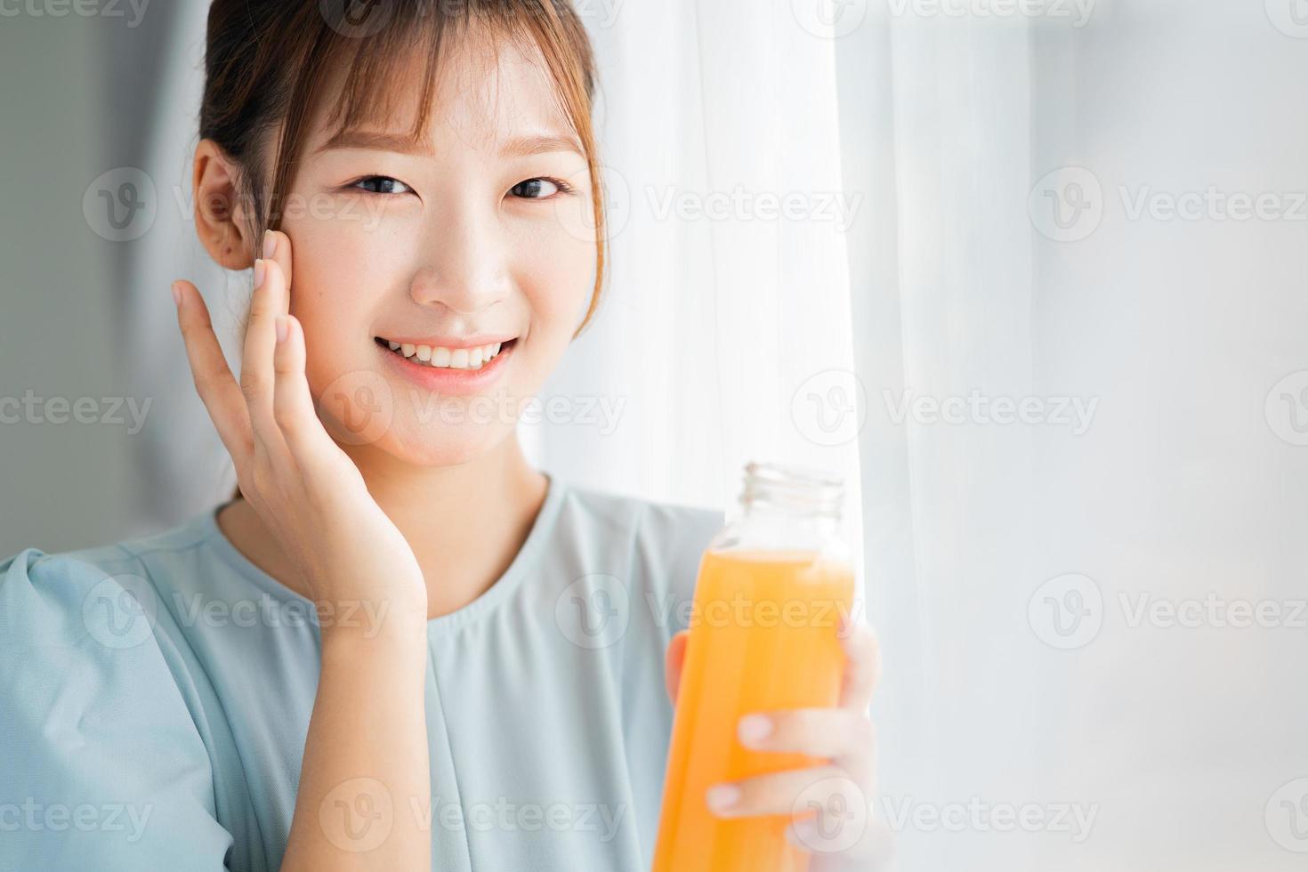 jeune femme asiatique boit du jus d'orange à côté de la fenêtre le matin photo