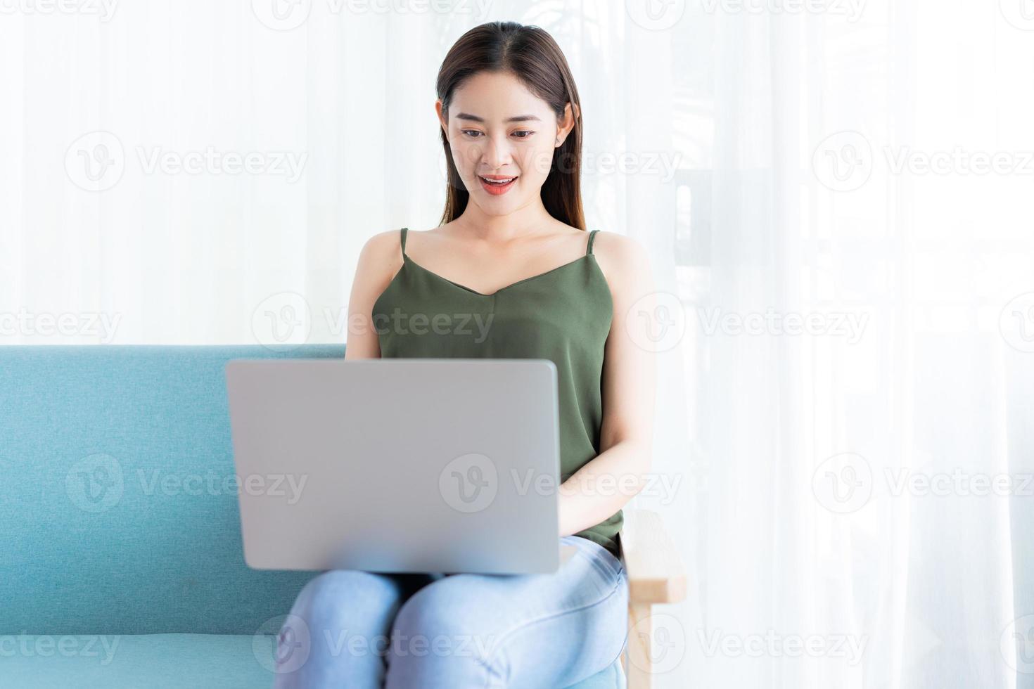 femme asiatique assise à l'aide d'un ordinateur portable sur un canapé photo