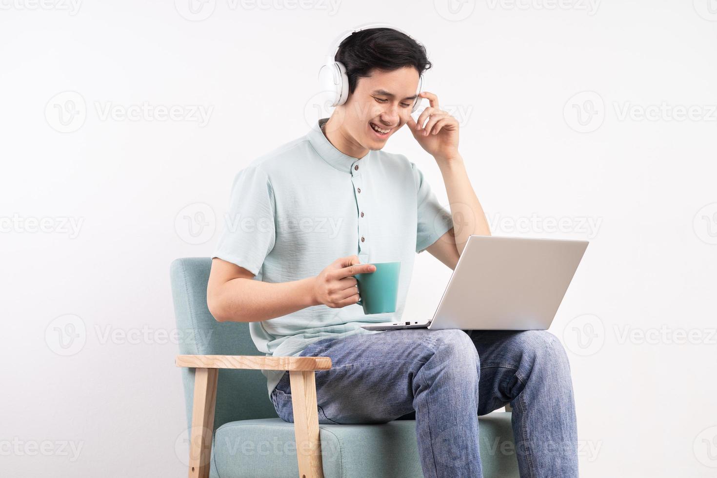 jeune homme assis sur le canapé écoutant de la musique et regardant l'écran de l'ordinateur avec une expression heureuse photo
