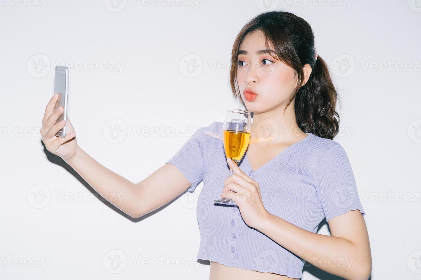 jeune femme asiatique buvant du vin et utilisant un smartphone sur fond blanc photo